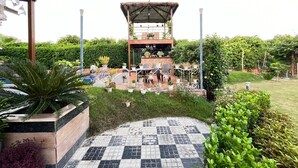 A patio area with a seating arrangement, potted plants, and a small structure with a roof. - GoBravo 37 - 2Bhk Farm with Pool & Garden Sec150 Noida (Noida)