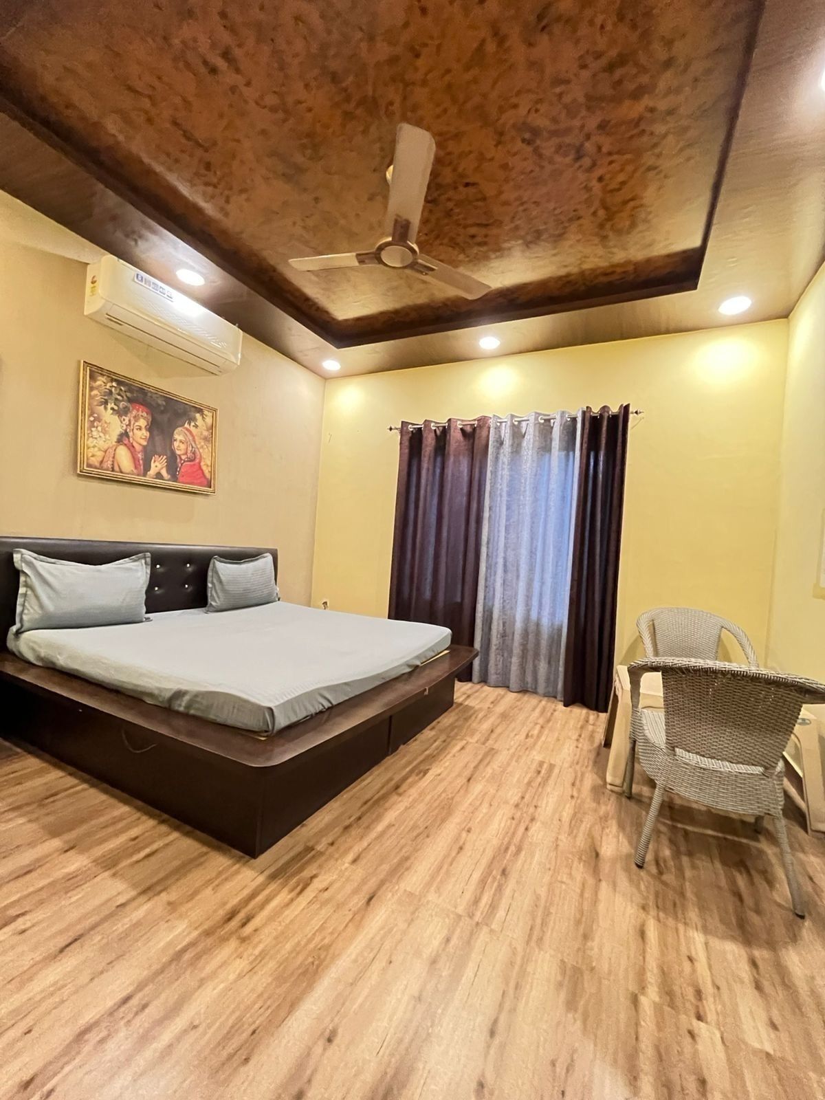 A bedroom with a bed, a chair, a ceiling fan, and a painting on the wall.