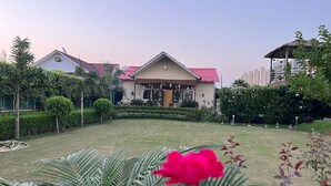 A house with a red roof, surrounded by well-maintained gardens and palm trees. - GoBravo 37 - 2Bhk Farm with Pool & Garden Sec150 Noida (Noida)
