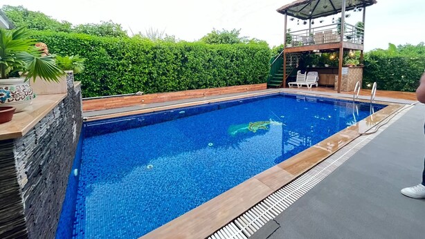 A rectangular swimming pool with a wooden deck and a covered seating area. - GoBravo 37 - 2Bhk Farm with Pool & Garden Sec150 Noida (Noida)