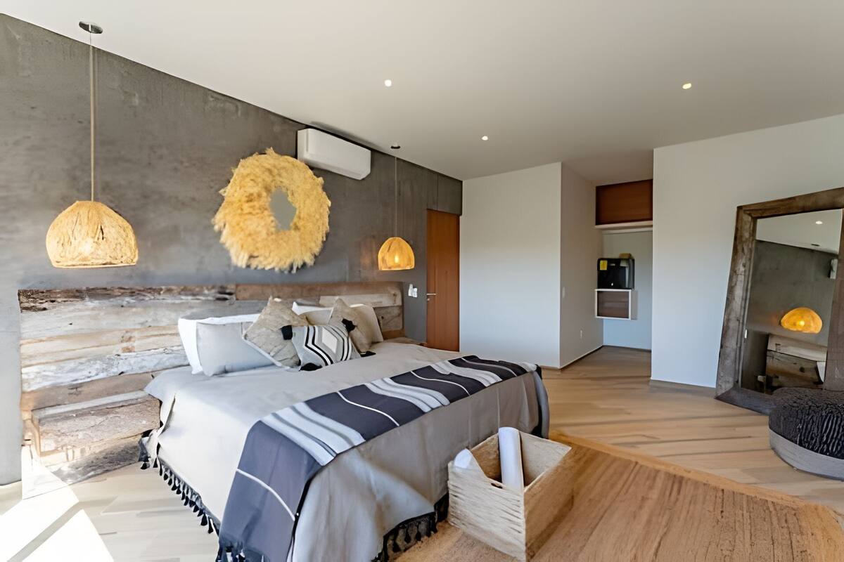 A modern bedroom with a large bed, a wooden headboard, and a rustic wall. There are two pendant lights and a round, textured wall decoration.