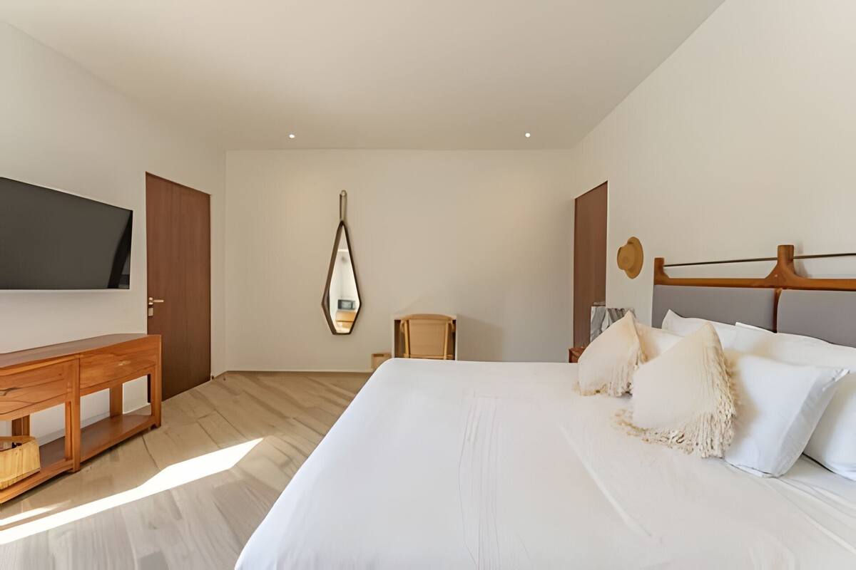 A bedroom with a bed, a wooden dresser, a chair, a mirror, and a television.