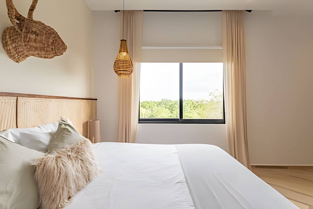 A bedroom with a large bed, a hanging basket, a lamp, and a window with curtains.