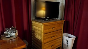 A wooden dresser with a television on top, a basket, and a table with a utensil holder.