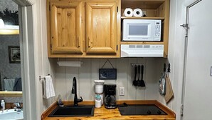 A compact kitchen with wooden cabinets, a microwave, a coffee maker, and a dishwasher.