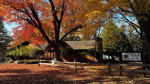 A private beach club with a wooden cabin, surrounded by autumn foliage and a stone chimney.