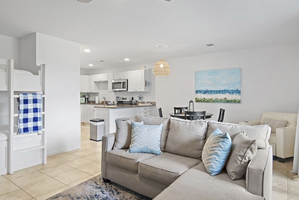A modern living room with a sofa, a dining table, and a kitchen in the background.
