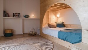 A cozy bedroom with a wooden arched ceiling, a bed with blue bedding, a round rug, and a shelf with decorative items. - Olivera, house in Rupià (Rupià)