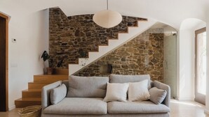 A modern living room with a grey sofa, a stone staircase, and a hanging light fixture. - Olivera, house in Rupià (Rupià)