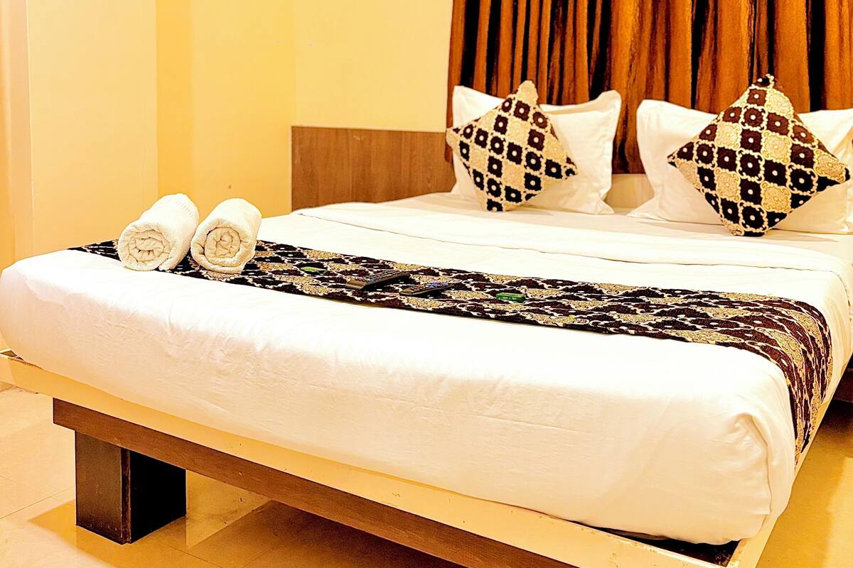 A hotel room with a bed, pillows, a blanket, and an air conditioning unit.