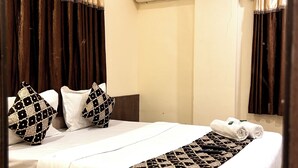 Una cama bien hecha con almohadas estampadas y una manta decorativa, un aire acondicionado de pared y cortinas oscuras.