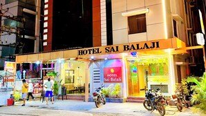 Un hotel llamado "HOTEL SAI BALAJI" con una fachada moderna, ventanas amplias y una entrada bien iluminada.