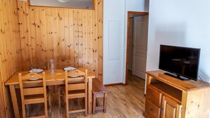 Un comedor de madera con una mesa y sillas, un televisor sobre un mueble de madera, y una puerta blanca al fondo.