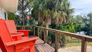 A wooden deck with a red chair, a railing, and a view of palm trees and greenery.