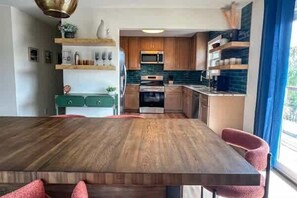 A modern kitchen with wooden cabinets, a central island, and a dining area with a wooden table and chairs. - Siren's Oasis 3 Bedroom Pet Friendly St George Island (St George Island)