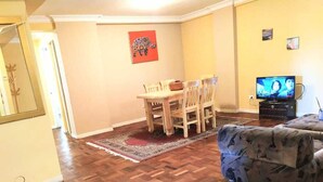A living room with a wooden herringbone floor, a dining area with a table and chairs, a sofa, and a television. - Charming 3-bedroom apartment in La Paz with AC, WiFi (La Paz)