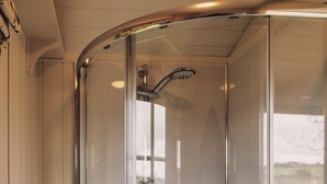 A glass-enclosed shower with a handheld showerhead and a handheld faucet.