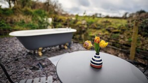 A bathtub, a round table with a striped vase, and a garden view.