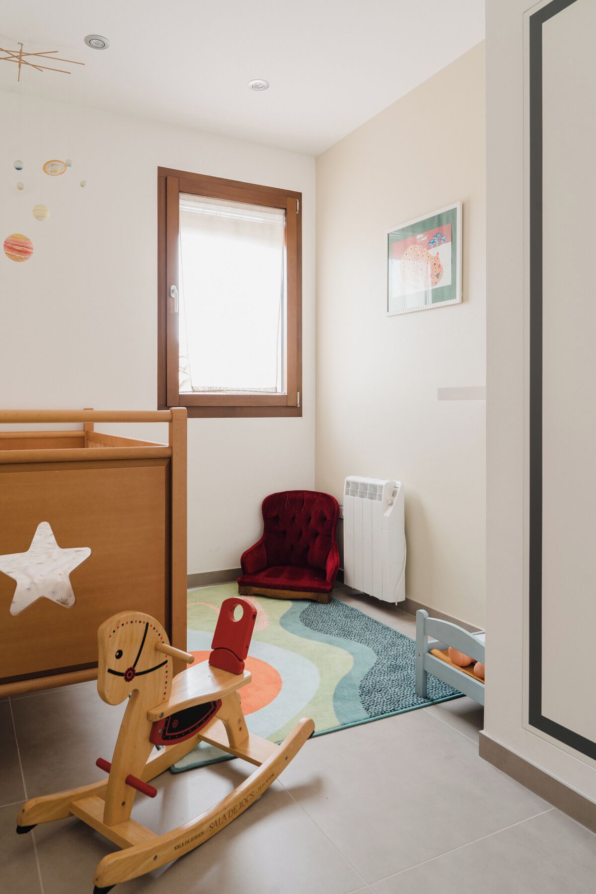 A child's playroom with a rocking chair, a red chair, a radiator, and a window with blinds.
