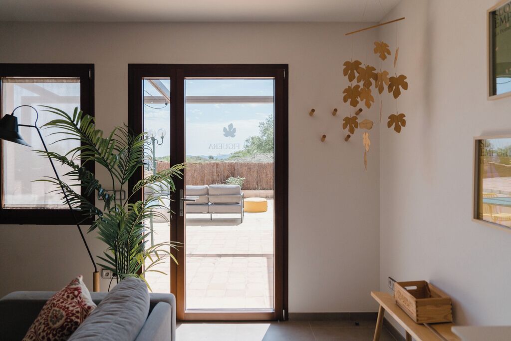 A modern living room with a sofa, a potted plant, and a sliding glass door leading to an outdoor patio area. - La Figuera, house at Ultramort (Ultramort)