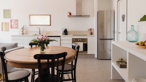 A modern kitchen with white cabinetry, a stainless steel refrigerator, and a wooden dining table with chairs. - La Figuera, house at Ultramort (Ultramort)
