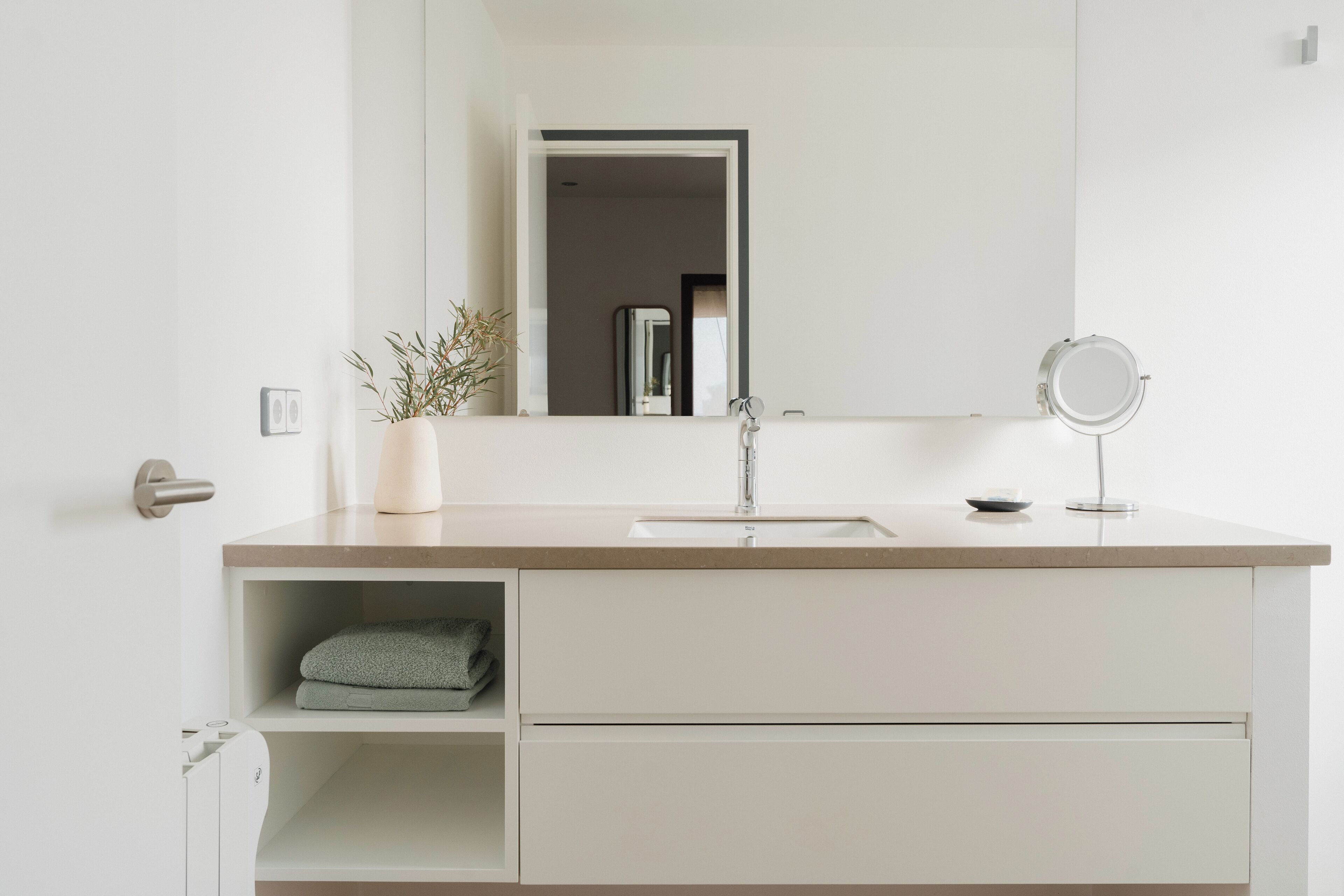 A modern bathroom with a white vanity, a mirror, and a potted plant.