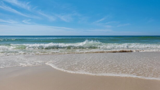 A beach with waves approaching the shore under a clear sky.