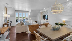 A spacious living area with a dining table, wicker furniture, and a modern chandelier.