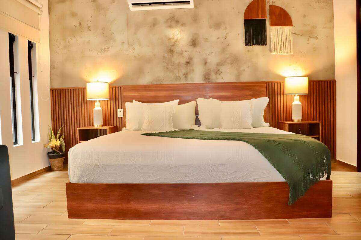 A large bed with a wooden headboard, two bedside lamps, and a green throw blanket.