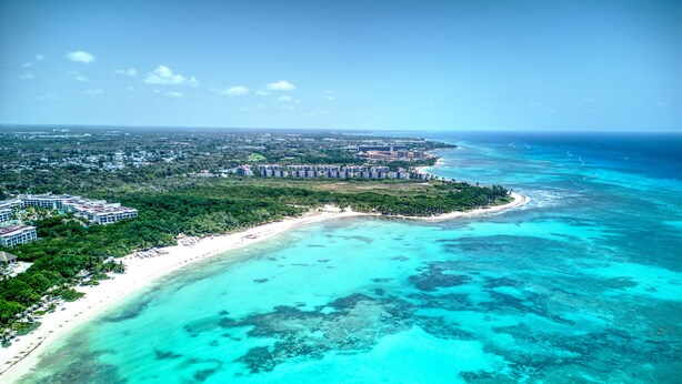 An aerial view of a coastal resort with a beachfront, dense greenery, and a clear blue sea. - Sunset Kin Beach Apartments (Playa del Carmen)