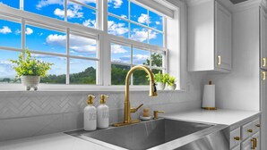 A modern kitchen with a stainless steel sink, white cabinetry, and a window with a view of the sky and trees.
