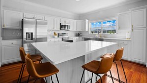 A modern kitchen with white cabinetry, stainless steel appliances, and a large island with bar stools.