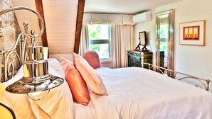 Ein Schlafzimmer mit Bett, Nachttisch mit Lampe, Kommode und Fenster mit Vorhängen.
