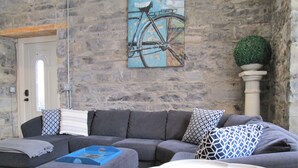 A living room with a stone wall, a sofa set, a coffee table, and a painting of a bicycle. - Luxury Limestone Suite is a Home Away from Home (KIngston)