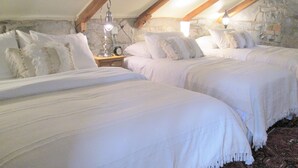 A bedroom with two beds, stone walls, wooden beams, and a nightstand with a lamp and clock. - Luxury Limestone Suite is a Home Away from Home (KIngston)