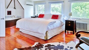 A spacious bedroom with a large bed, a wooden floor, a cowhide rug, and a view of trees through the window. - 18th Century Luxury Suite with Rustic Charm (KIngston)