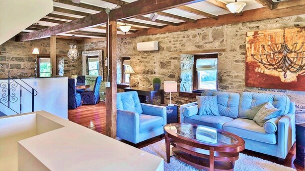 A spacious living area with a stone wall, wooden beams, a large chandelier, and a blue sofa set. - 18th Century Luxury Suite with Rustic Charm (KIngston)