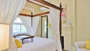 Un lit à baldaquin avec une literie blanche, une chaise blanche avec un coussin jaune et une cheminée blanche.