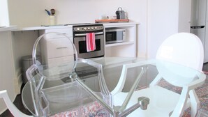 Une cuisine moderne équipée d’un four, d’un micro-ondes et d’une armoire blanche au-dessus. On y trouve une table en verre avec des chaises, ainsi qu’une chaise blanche dans l’espace repas.