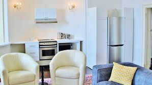 Un espace de vie compact comprenant un coin cuisine, deux fauteuils, un canapé agrémenté d’un coussin à motifs et un appareil électroménager de grande taille.