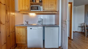 Eine kompakte Küche mit Holzausstattung, einer Mikrowelle, einer Kaffeemaschine und einem Geschirrspüler.
