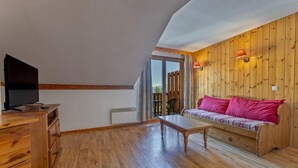 Ein Wohnzimmer mit Holzboden, einer Couch, einem Couchtisch und einem Fernseher auf einer Holzkommode.