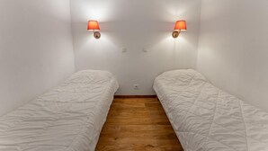 A narrow room with two single beds, each with a white duvet, wooden flooring, and two wall-mounted lamps with red shades. - 40m from ski slopes, 3rd floor, fitness, swimming pool, sauna, tv, ski locker, 35m², Les Orres (Les Orres)