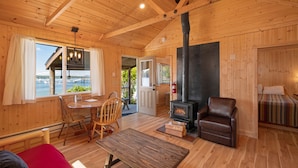 Interior acogedor de una cabaña con piso de madera, chimenea, comedor y vista al agua.