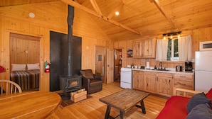 Interior de una cabaña de madera con comedor, sofá, chimenea, cocina y un sofá rojo.