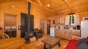 A wooden cabin interior with a dining area, a sofa, a fireplace, a kitchen, and a red couch.