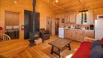 A wooden cabin interior with a dining area, a sofa, a fireplace, a kitchen, and a red couch.