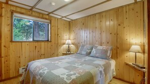 Dormitorio con paneles de madera, una cama grande, dos lámparas de noche y un ventanal con vista a árboles.