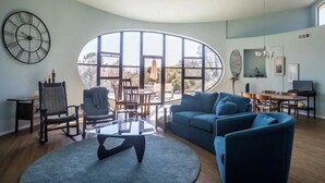 Un salon spacieux doté d’une grande fenêtre ovale, d’un canapé moderne, d’une table basse en verre et d’un coin repas agrémenté d’un lustre.