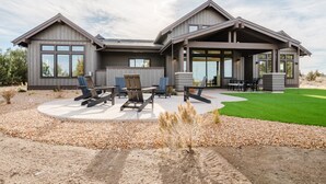 A modern two-story house with a covered patio area, outdoor seating, and a well-maintained lawn.